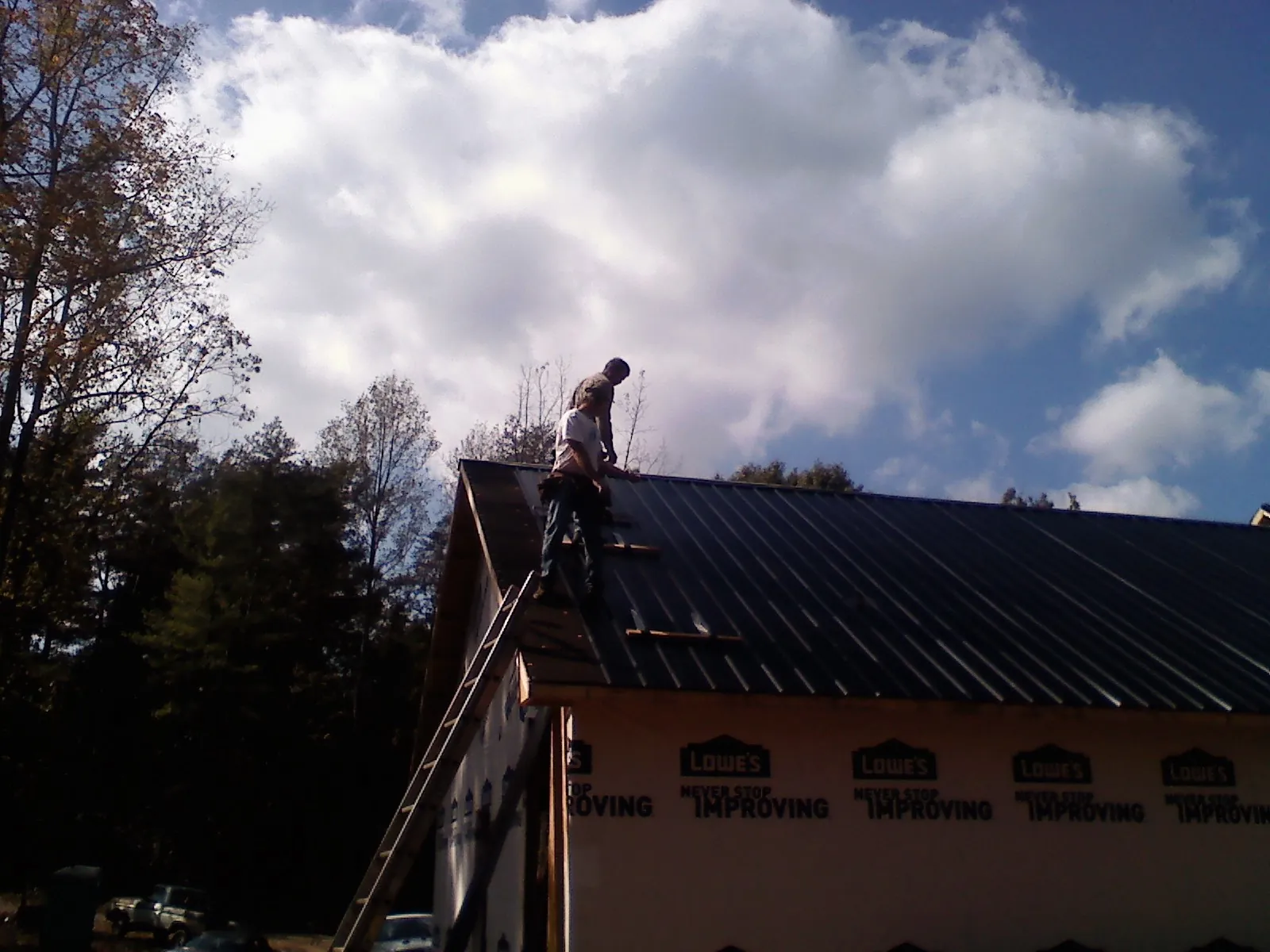 Roofer fastening dark metal panels high against a cloudy sky, from a Roof Inspection job in Morristown